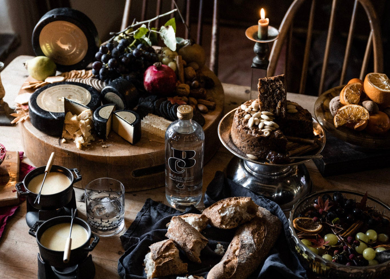 Table setting with cheeseboard, bread, drinks, and decorative items in a warm, dimly lit room.
