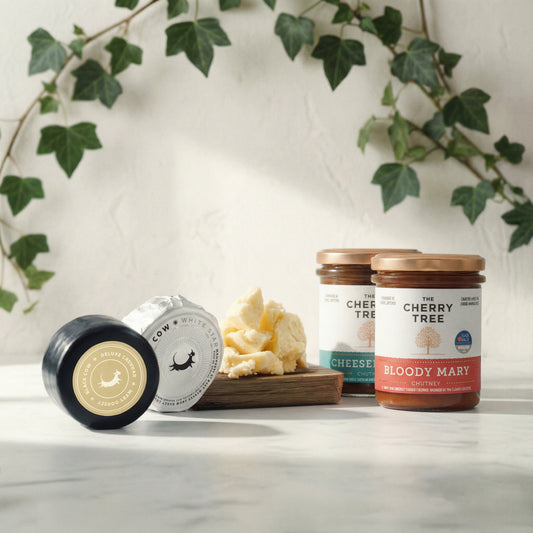 Jars of chutney and blocks of cheese on a marble surface with a decorative plant in the background.