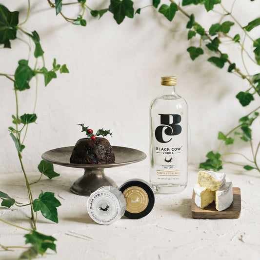 Bottle of Black Cow vodka with a Christmas pudding and cheese on a decorative setting.